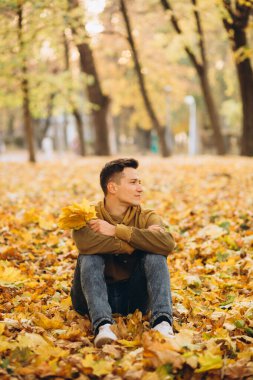 Bir buket sarı yapraklı yakışıklı ve mutlu çocuğun portresi gülerek sonbahar parkında hayal kuruyor.