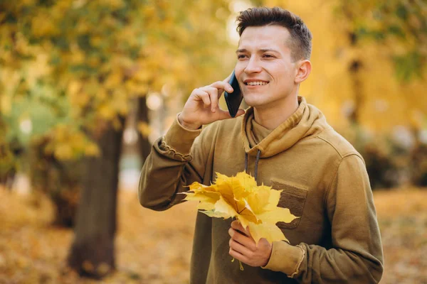 ハンサムな幸せな男の肖像画笑顔と秋の公園で電話で話して — ストック写真