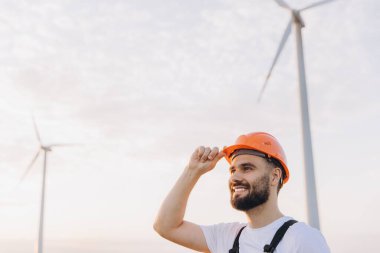 Arab engineer adjusting his helmet while working at a wind turbine farm, embodying the essence of renewable energy and sustainable practices
