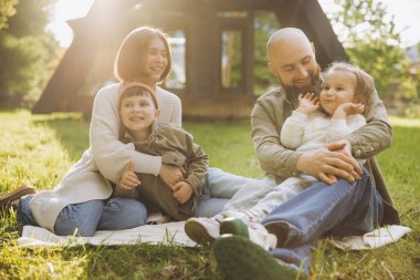 Parents hugging children while sitting on blanket in backyard, enjoying sunny day and expressing love and togetherness