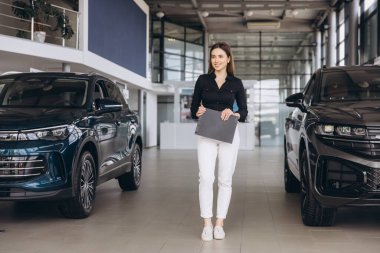 Saleswoman holding folder standing between two cars in a dealership