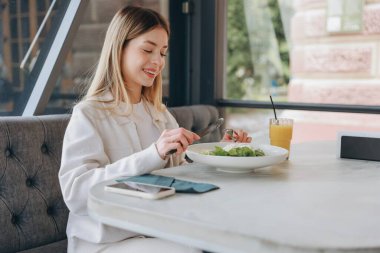Young woman enjoying a fresh salad and sipping orange juice while seated at a restaurant, embracing a healthy lifestyle during lunch