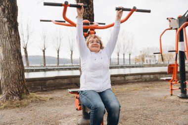 Elderly woman exercising on outdoor fitness equipment, promoting healthy lifestyle and active aging by the lake