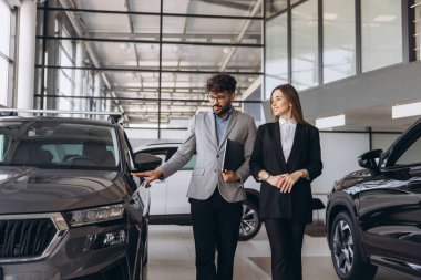 Salesperson showing features of a new car to a businesswoman in a car dealership, discussing purchase options