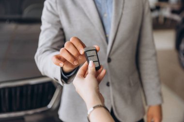 Car salesman handing car keys to a client in a vibrant dealership after finalizing the contract, marking a successful transaction