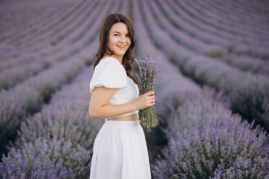 Young woman holding a bouquet of freshly picked lavender in a beautiful lavender field, enjoying the scent and the colors of nature
