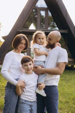 Smiling family embracing in front of their new sustainable a frame house, enjoying their life together