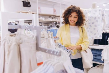 Smiling curly haired woman shopping for clothes, enjoying her buying experience in a fashion store