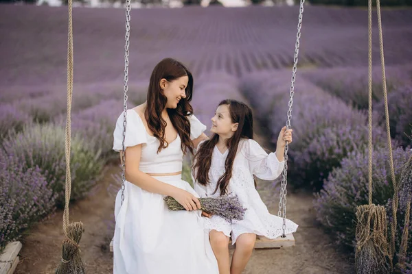 Mother and daughter wearing white dresses are swinging and holding a lavender bouquet in a beautiful lavender field