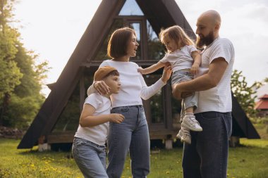 Happy family with two children having fun in front of their modern a frame house in the countryside