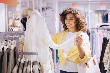 Customer enjoying a shopping experience, examining a stylish garment in a clothing store, radiating happiness over a recent purchase
