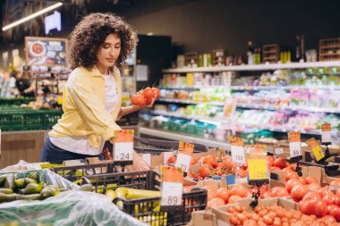 Young woman selecting ripe tomatoes in a grocery store, enjoying the process of choosing fresh vegetables for a nutritious diet