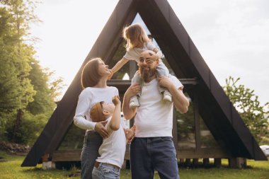 Family of four enjoying quality time outside their modern a frame house, basking in the warm glow of the sunset light