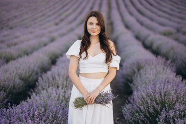 Fashion model posing gracefully in a vibrant lavender field, holding a beautiful bouquet of fresh lavender flowers in her hands