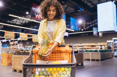 Smiling customer selecting fresh pineapple, enjoying grocery shopping experience in modern supermarket