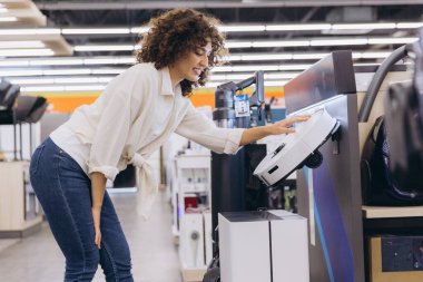 Customer examining a modern robot vacuum cleaner in an appliance store, considering a purchase for home cleaning