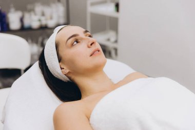 Client lying on a massage table with a towel on her head, enjoying a moment of relaxation during a beauty treatment in a professional cosmetology clinic