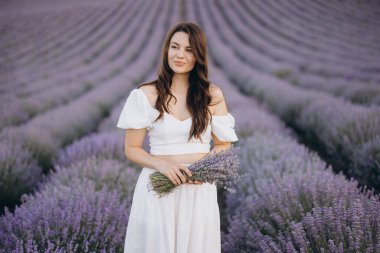 Young woman in a flowing white dress, holding a vibrant bouquet of lavender flowers while surrounded by a breathtaking lavender field