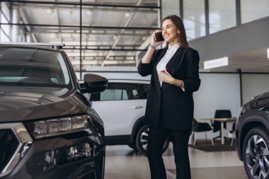 Saleswoman engaging in a phone conversation, skillfully selling a new car at a bustling car dealership showroom, exuding professionalism and confidence