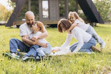 Family enjoying quality time in their garden, laughing, playing, and embracing each other on a cozy blanket under the sun