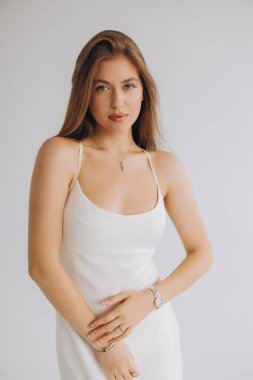 Studio portrait of a young woman with long brown hair wearing a white dress and silver jewelry