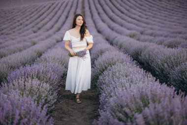 Young woman walking gracefully through a vibrant lavender field, holding a beautiful bouquet of fresh lavender flowers in hand