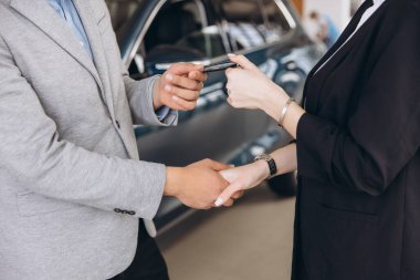Car salesman handing over car keys to a satisfied customer at the dealership, celebrating the successful closing of a new vehicle deal