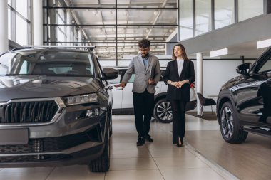 Salesman showing a new car to a potential customer in a car dealership, discussing features and financing options