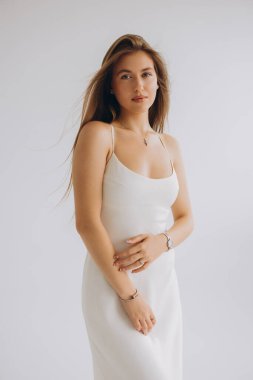 Fashion model posing gracefully in an elegant white dress and stunning jewelry, set against a clean, bright studio background