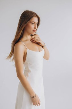 Fashion model posing wearing elegant white dress with thin straps and accessories, looking to the side