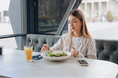 Young woman looking at a fresh salad with mozzarella and orange juice on a table in a restaurant