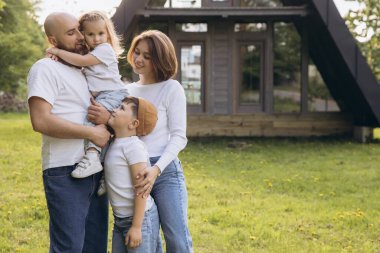 Smiling family with two children standing together in the garden of their new home, enjoying a sunny day