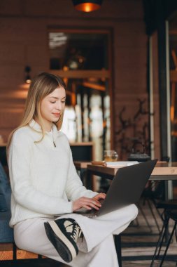 Freelancer enjoying a cup of tea while working remotely from a cozy cafe, typing on her laptop and soaking in the natural light