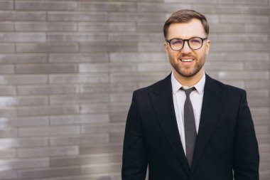 Portrait of a businessman smiling and wearing a suit and tie while standing in front of a brick wall