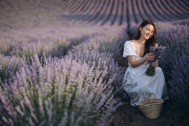 Young woman in white dress picking lavender flowers in a field at sunset, creating a peaceful and aromatic scene