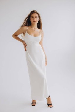 Fashion model posing gracefully in a flowing white dress and sleek black high heels against a minimalist white background
