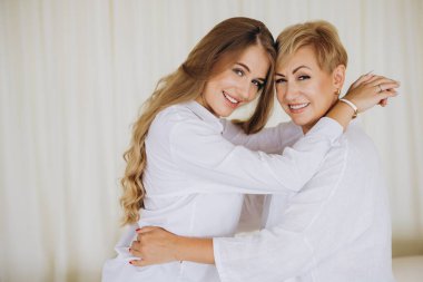 Mother and daughter in white shirts hugging and smiling, cherishing their special bond and enjoying a joyful moment together