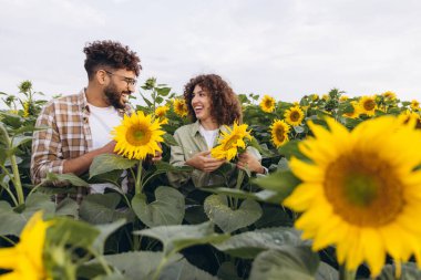 Two agronomists smiling while examining vibrant sunflowers in a sunny field, collaborating on agricultural insights and quality checks