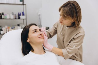 Beautician marking injection points on woman's face before botulinum toxin injections in beauty clinic