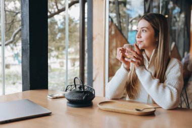 Freelancer enjoying a cup of tea in a cafe, working remotely with her laptop and taking a break