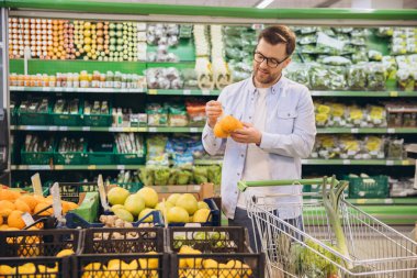 Customer selecting fresh oranges in grocery store, shopping for healthy food