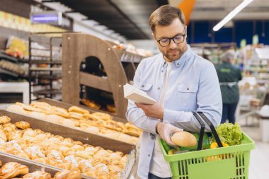 Customer wearing gloves choosing bread and checking shopping list in a supermarket