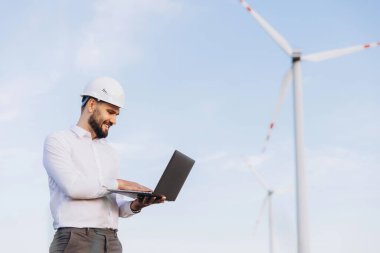 Engineer is using a laptop in a wind turbine power plant, controlling sustainable energy production