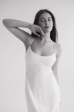 Young woman with long hair wearing white dress and posing with closed eyes and hand on her face