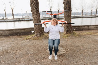 Elderly woman exercising on outdoor gym equipment, promoting healthy aging and active lifestyle by the lake