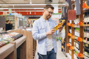 Customer reading label of wine bottle while shopping in supermarket alcohol section