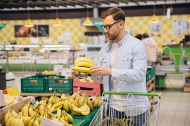 Customer buying bananas in grocery store, holding a bunch and looking at the quality of the fruit