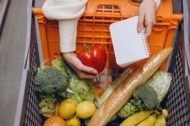 Market alışverişi yaparken kırmızı biber ve alışveriş listesi tutan bir kadın.