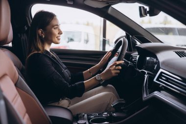 Yeni arabasında oturan iş kadını elinde direksiyonla araba galerisinde gülümsüyor.