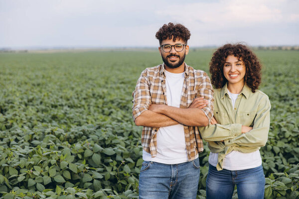 Two agronomists standing confidently with arms crossed in a lush soybean field, smiling proudly amidst the vibrant green crops